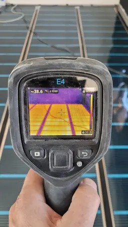 Pomiar temperatury rozłożonej maty grzewczej za pomocą kamery termowizyjnej, widoczny ekran urządzenia z nałożonym obrazem termicznym.