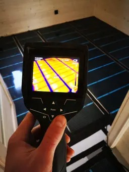 Pomiar temperatury maty grzewczej termowizją; widok z kamery termowizyjnej na rozłożoną matę na podłodze w trakcie montażu.