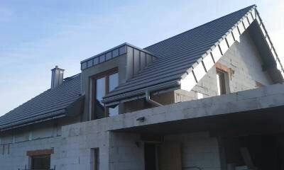 Nowy, grafitowy dach z dachówki ceramicznej na domu w trakcie budowy, widoczne obróbki blacharskie i rynny, surowy stan elewacji.