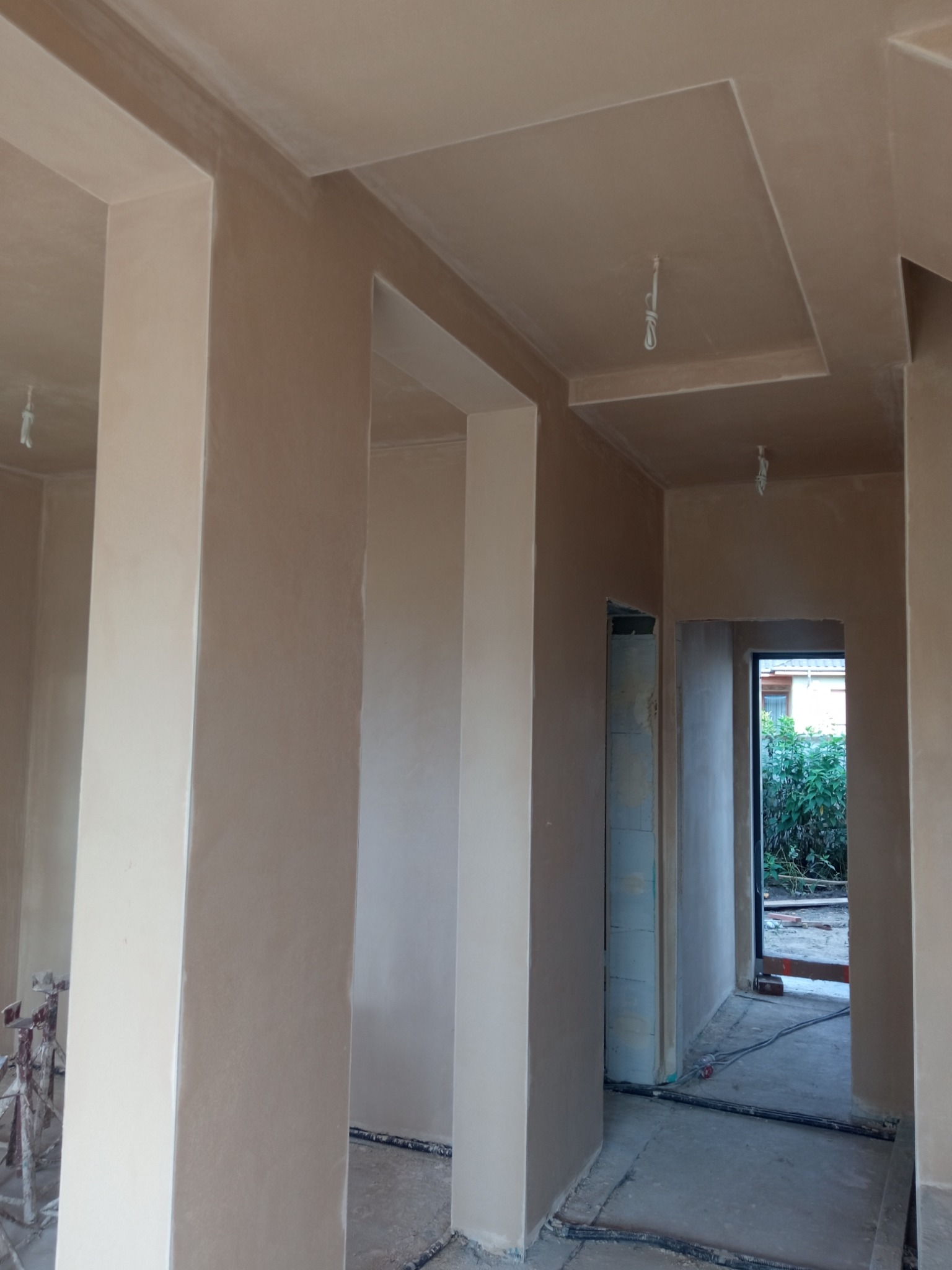 Wnętrze po tynkowaniu maszynowym: gładkie ściany i sufity w surowym wykończeniu, widoczne przewody elektryczne, stojak malarski w rogu. Detal: dekoracyjny sufit.