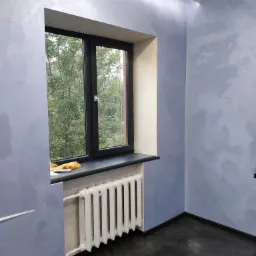 Pokój po malowaniu ścian na niebiesko z efektem dekoracyjnym, widoczny grzejnik, czarne okno z widokiem na zieleń i ciemna podłoga.