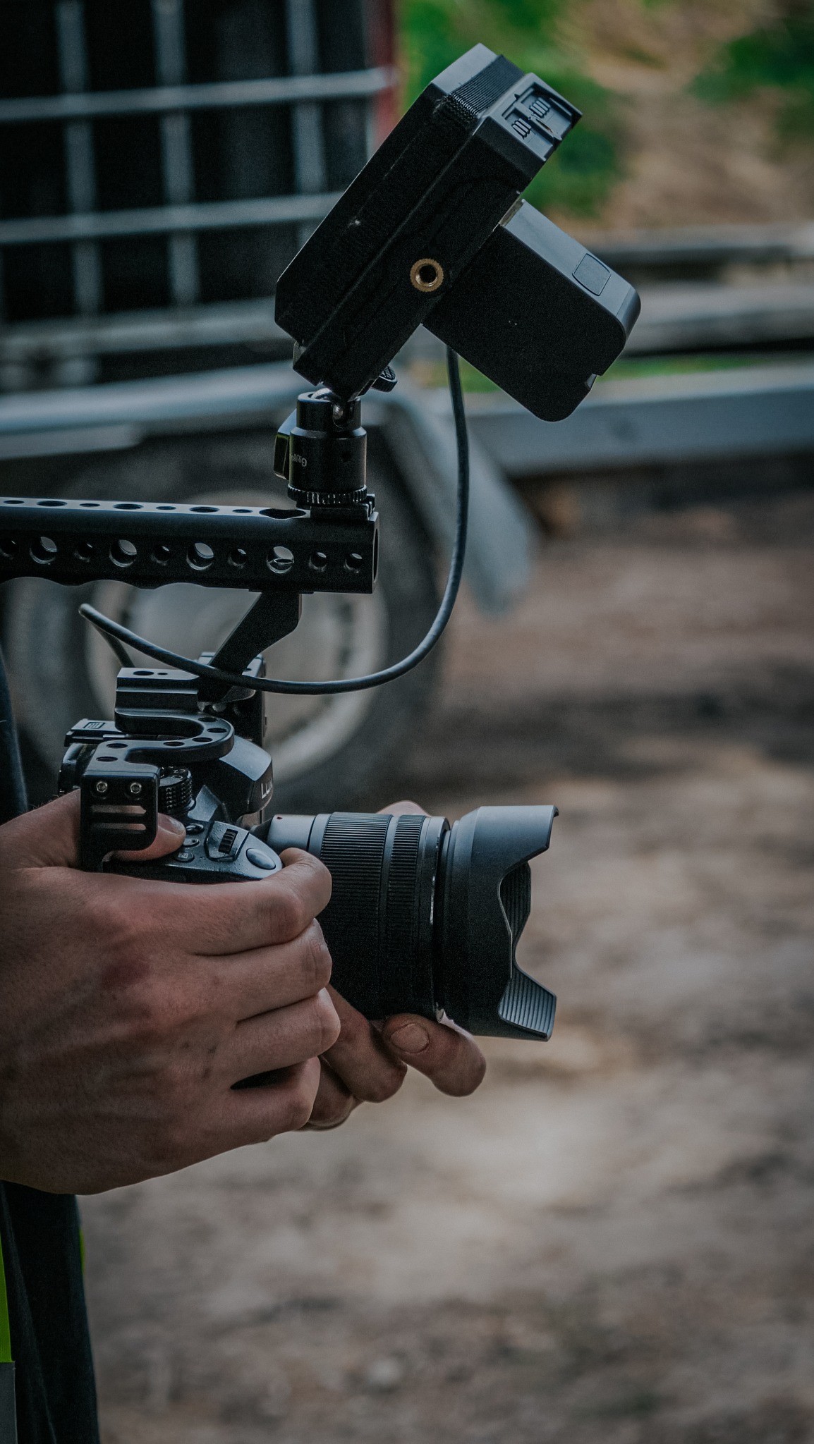 Profesjonalny aparat z mikrofonem i uchwytem w dłoniach, ustawiony do nagrywania, z przyczepką w tle.