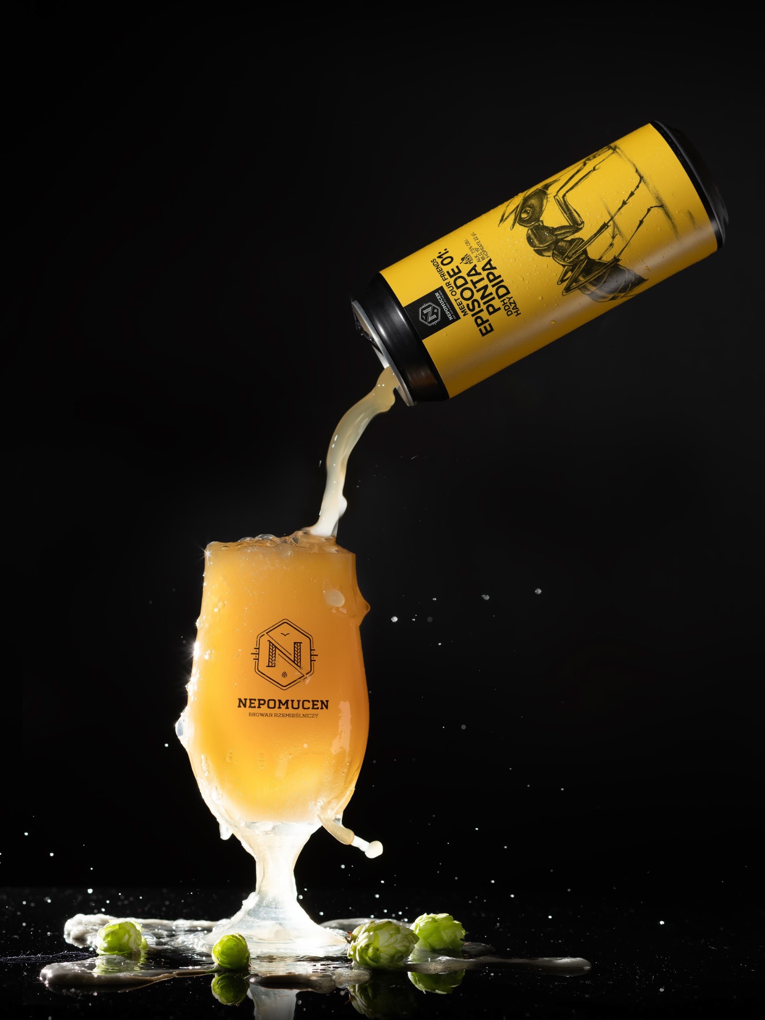 Żółta puszka piwa rzemieślniczego z rysunkiem mrówki lejąca zawartość do szkła z logiem Nepomucen na czarnym tle, widoczne chmielowe szyszki.