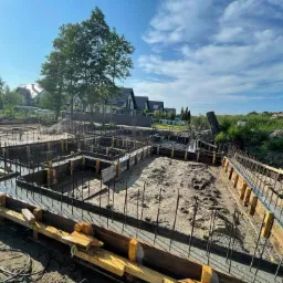 Wylane fundamenty zbrojone stalą, przygotowane pod budowę domu w Wierzchosławicach, widok na konstrukcję szalunkową w słoneczny dzień.