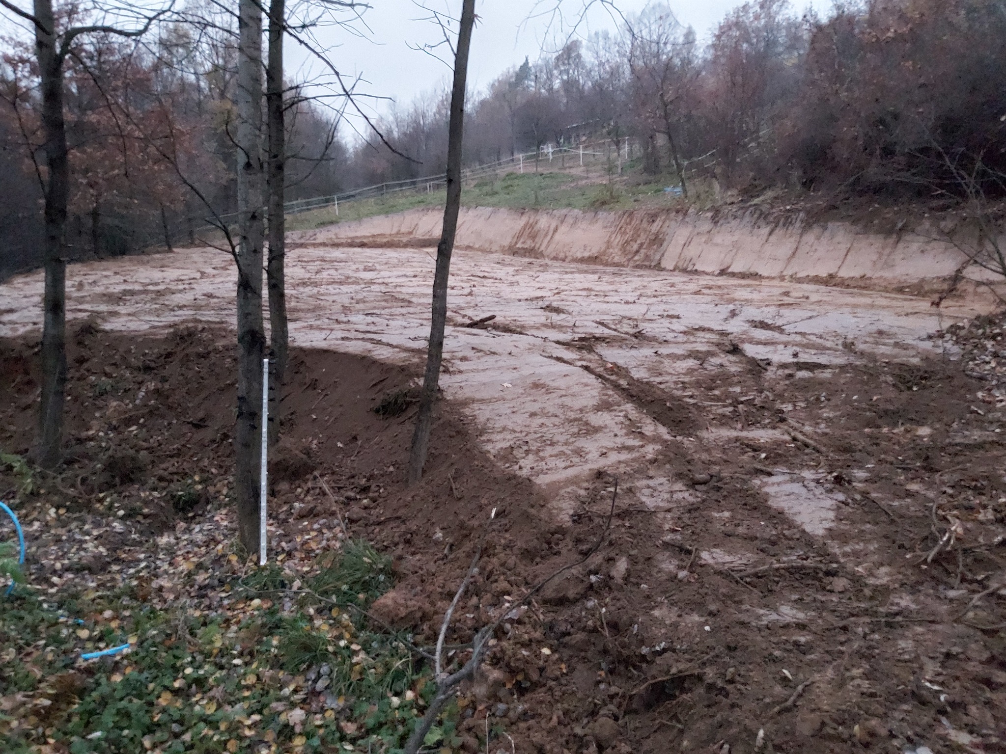 Przygotowany teren pod ujeżdżalnię koni z widocznymi śladami opon, otoczony drzewami i z wyraźnie zarysowanymi krawędziami wykopu.