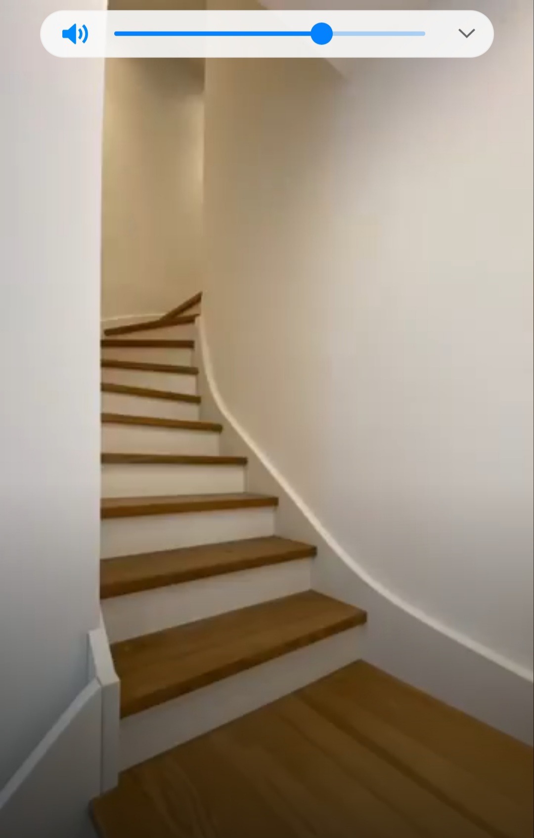 Klatka schodowa z drewnianymi stopniami i białymi podstopnicami, zakręcająca w lewo, widok od dołu.