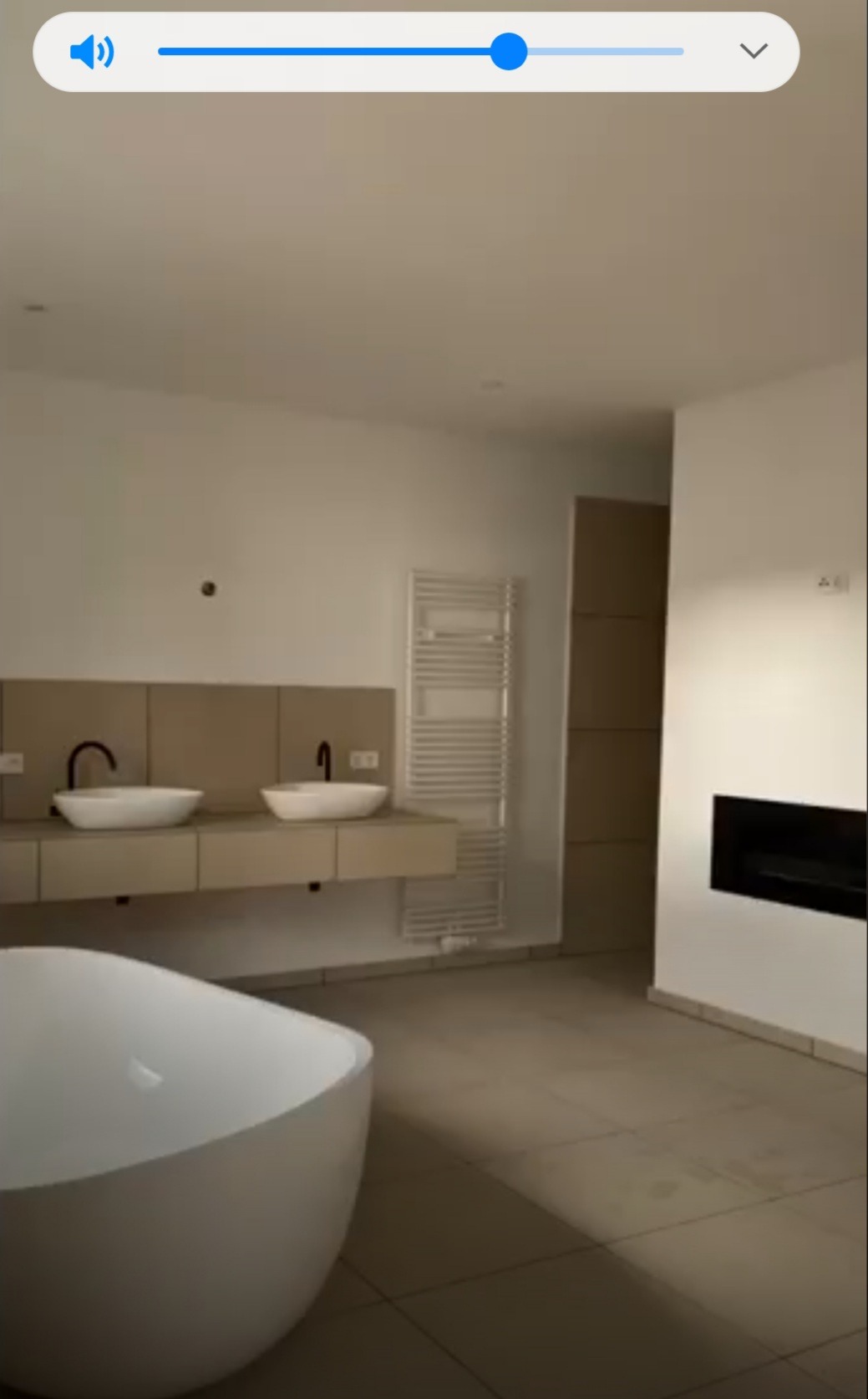 Nowoczesna łazienka z wolnostojącą wanną, dwoma umywalkami nablatowymi z czarnymi bateriami, grzejnikiem drabinkowym i kominkiem w minimalistycznym stylu.