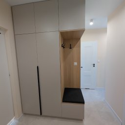 Fado Wood - Jasna szafa wnękowa z siedziskiem i wieszakami w przedpokoju. Minimalistyczny design, gładkie fronty, czarne uchwyty. Drewniane wykończenie wnęki.