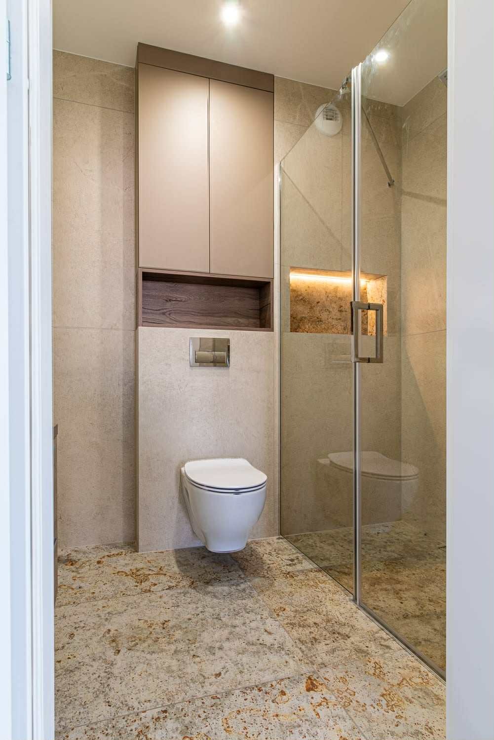 Nowoczesna łazienka z szafką na wymiar w Łodzi. Beżowe płytki, podświetlana wnęka i szklana kabina prysznicowa tworzą spójną całość.