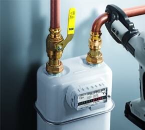 Biały gazomierz z mosiężnymi zaworami i miedzianymi rurami, połączony z zaciskarką do rur. Szare tło ściany. Widok z bliska, ostre światło.