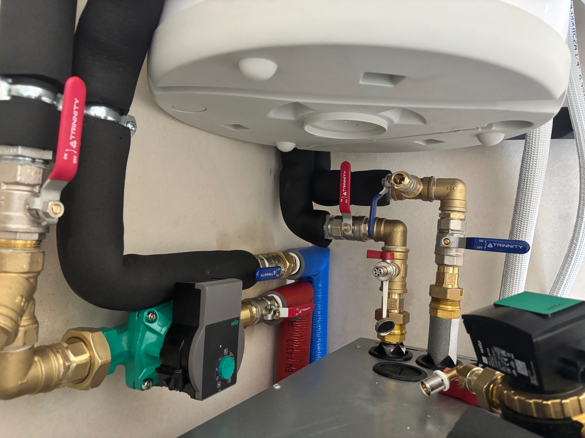 Nowoczesny piec gazowy z widocznymi rurami, zaworami i pompą obiegową. Elementy instalacji w kolorach: czarnym, czerwonym, niebieskim i zielonym.