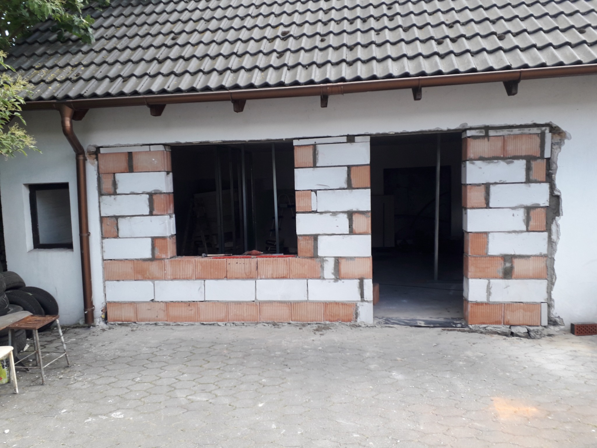 Wymurowane otwory okienne i drzwiowe z bloczków silikatowych i czerwonej cegły na elewacji budynku z szarym dachem, widok na wnętrze budynku.