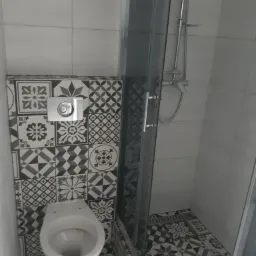 Nowoczesna łazienka z kabiną prysznicową i podwieszaną toaletą, wykończona płytkami w stylu patchwork w odcieniach szarości i bieli.