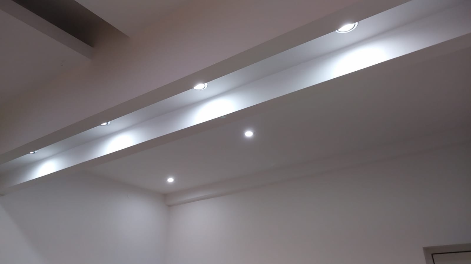 Białe wnętrze pokoju z podwieszanym sufitem i wpuszczonym oświetleniem punktowym LED, widok od dołu.