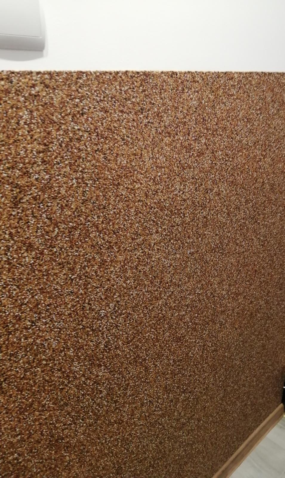 Brązowa ściana pokryta dekoracyjnym tynkiem mozaikowym, widoczny fragment białego sufitu i listwa przypodłogowa.