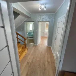 Korytarz po remoncie z drewnianą podłogą, schodami i ozdobną strukturą na ścianach, widok zza otwartych drzwi.