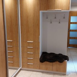 Paweł Gębura - Wnętrze przedpokoju z zabudową na wymiar: szafa przesuwna z lustrem, komoda z szufladami i wnęka z siedziskiem wyłożonym futrem, oświetlona lampą disco.