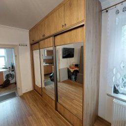 Paweł Gębura - Jasna szafa wnękowa z lustrami, drewnopodobne wykończenie, przesuwne drzwi. Widok na wnętrze mieszkania w odbiciu luster.