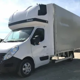 Biały samochód dostawczy Renault Master z plandeką i kabiną sypialną, zaparkowany na żwirowym placu.