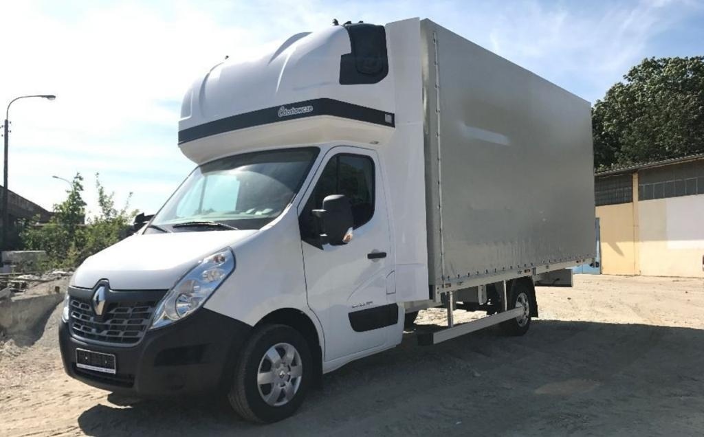 Biały samochód dostawczy Renault Master z plandeką i kabiną sypialną, zaparkowany na żwirowym placu.