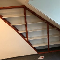 Mpower Remonty - Zabudowa wnęki na poddaszu z drewnianym regałem z białymi półkami, widoczne niedoskonałości wykończenia przy ścianie.