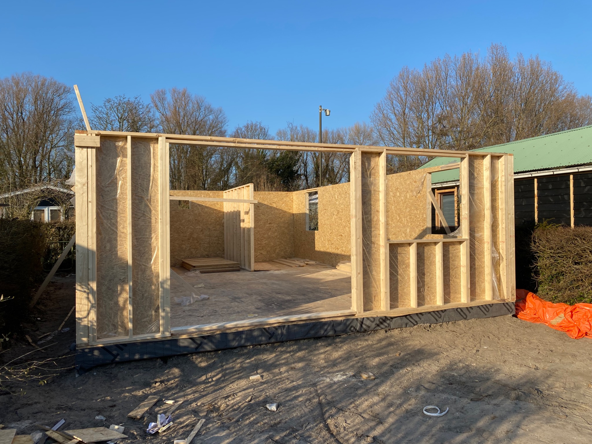 Wczesny etap budowy drewnianej altany lub domku letniskowego: surowe ściany z płyty OSB na drewnianym szkielecie, widoczne elementy konstrukcyjne i brak wykończenia zewnętrznego.