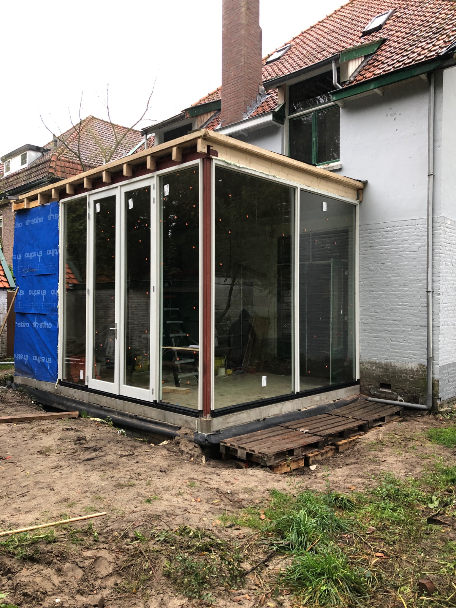 Budowa przeszklonej werandy w Wałbrzychu: widoczne elementy konstrukcyjne, drewniane belki i duże przesuwne okna, teren wokół w trakcie prac ziemnych.