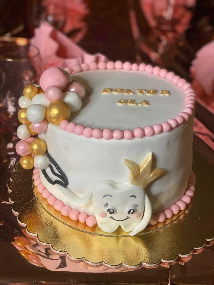 Tort urodzinowy dla dentystki, z napisem 'Doktor Ola', dekorowany motywem zęba w koronie i pastelowymi kuleczkami.