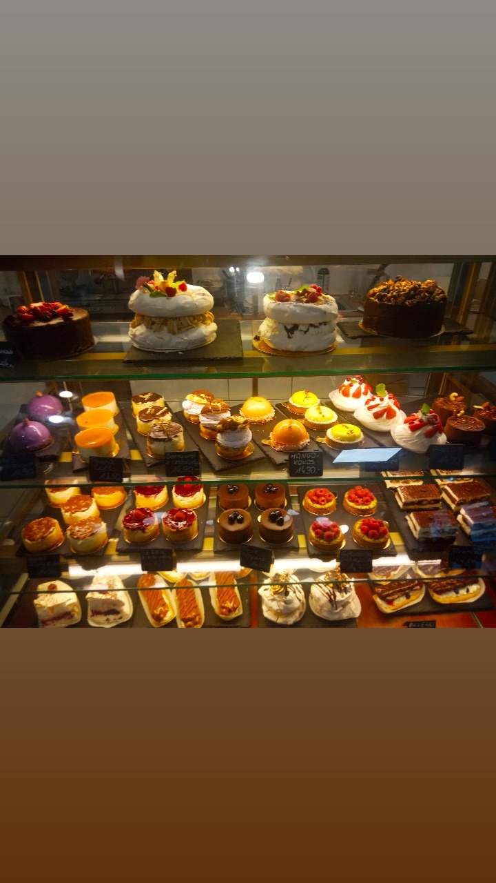 Słodki bufet w cukierni: torty bezowe, monoporcje musowe, eklerki i tartaletki z owocami w szklanej gablocie.