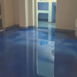 Błyszcząca, ciemnoniebieska podłoga w pokoju z białymi ścianami i kolumnami, widoczne odbicie wnętrza łazienki w podłodze.