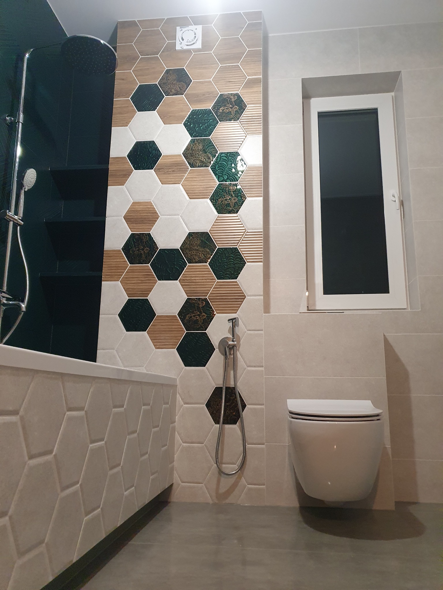 Nowoczesna łazienka z heksagonalnymi płytkami w odcieniach bieli, drewna i zieleni, kabina prysznicowa typu walk-in, podwieszana toaleta i okno z białymi ramami.