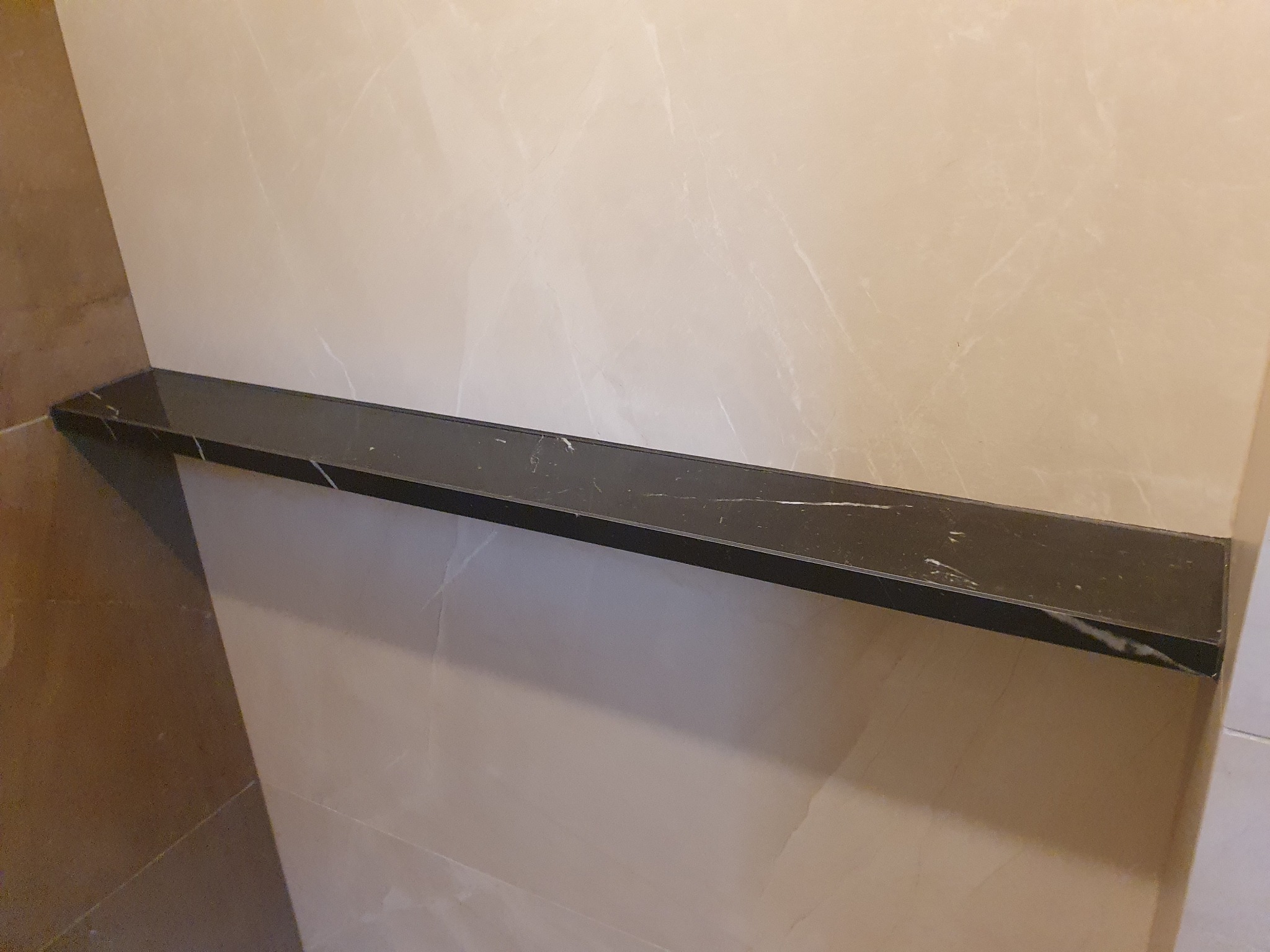 Półka z czarnego marmuru zamontowana na ścianie z beżowych płytek w łazience, widok z dołu.