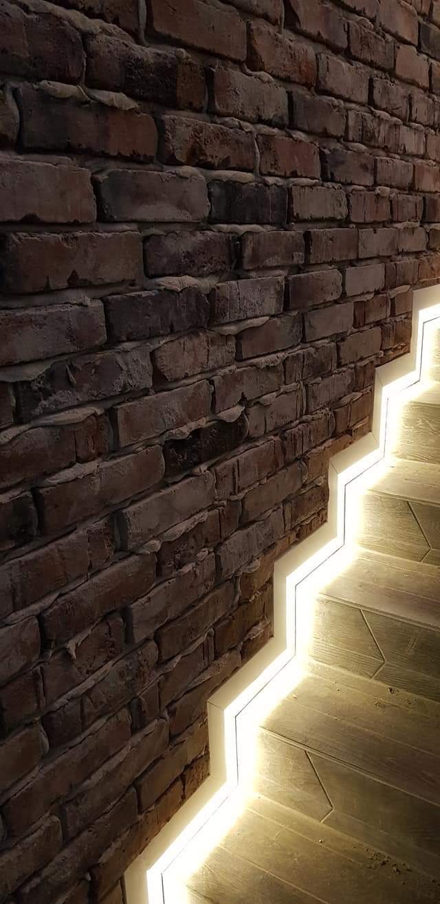 Ceglana ściana z oświetleniem LED schodów, widok z dołu, ciepłe światło.
