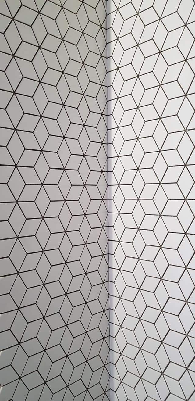 Ściana i narożnik wyłożone białymi, trójwymiarowymi płytkami w kształcie rombów z ciemnoszarą fugą, tworzące geometryczny wzór.