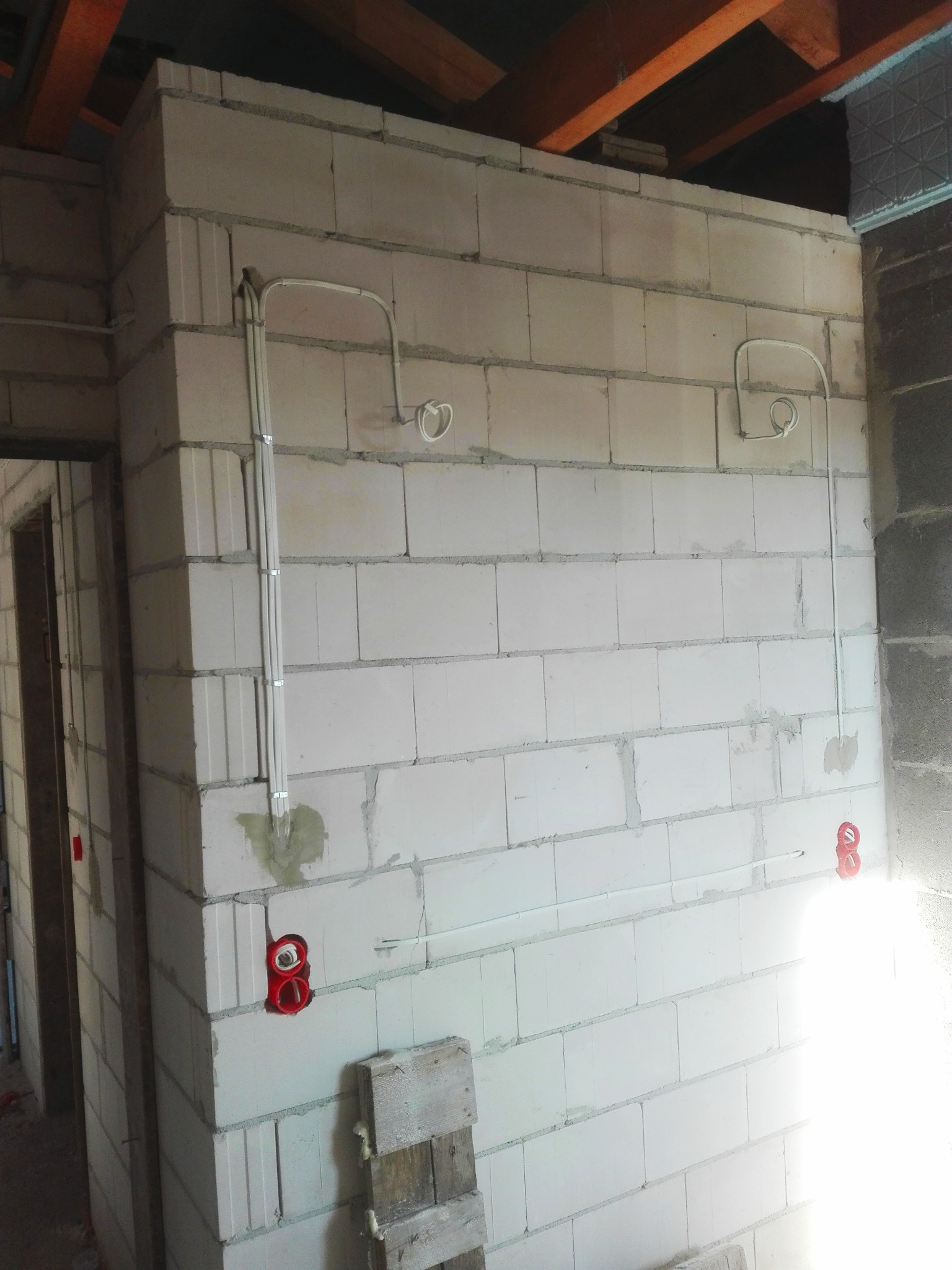 Surowa ściana z betonu komórkowego z widocznymi przewodami elektrycznymi w peszlach i puszkami instalacyjnymi, przygotowana do dalszych prac wykończeniowych.