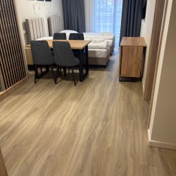 DIR Company Montaż Podłóg - Jasne panele podłogowe w pokoju hotelowym z łóżkiem, stołem i krzesłami. Widoczne detale tekstury paneli i aranżacja wnętrza.
