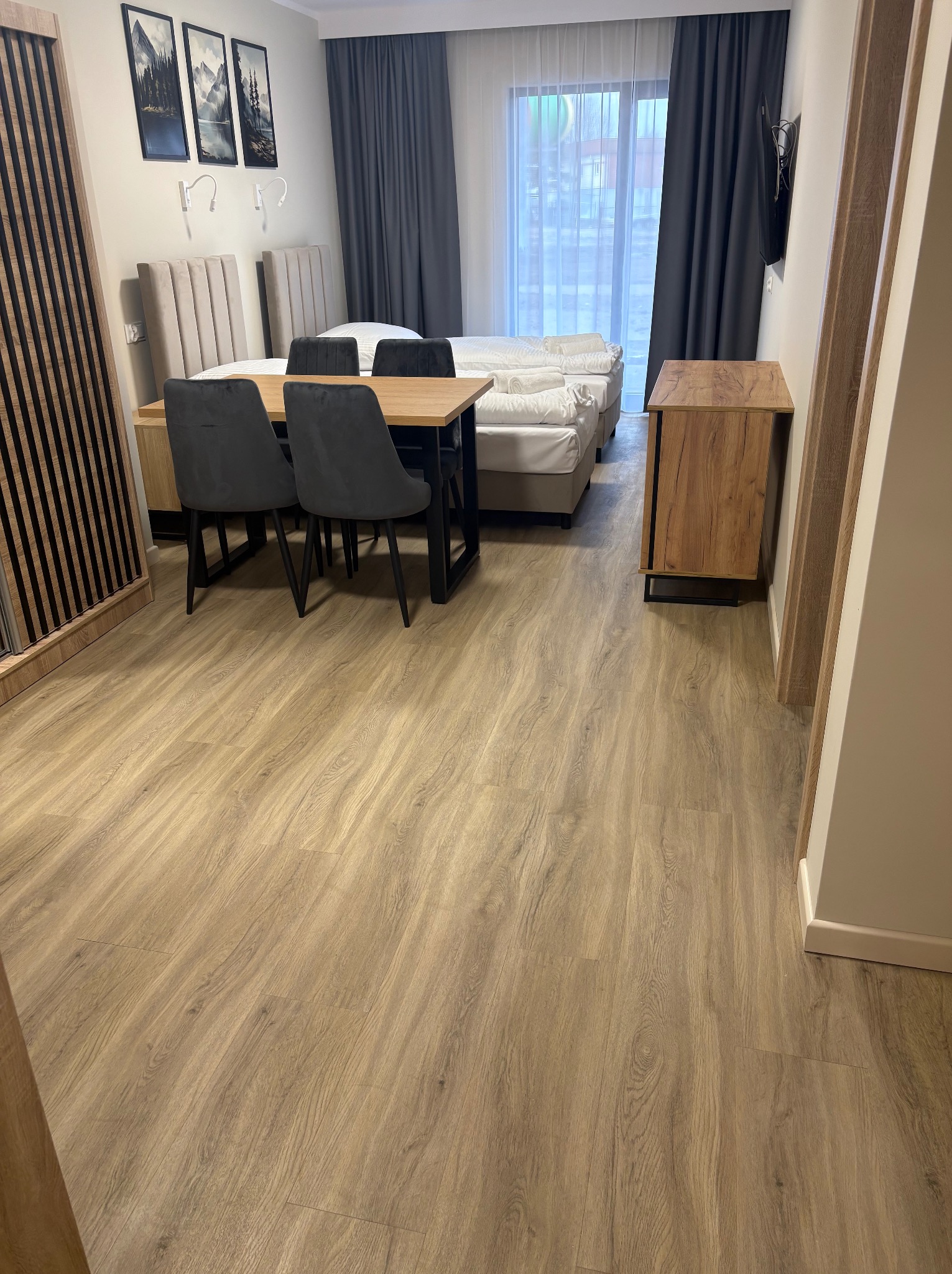 Jasne panele podłogowe w pokoju hotelowym z łóżkiem, stołem i krzesłami. Widoczne detale tekstury paneli i aranżacja wnętrza.