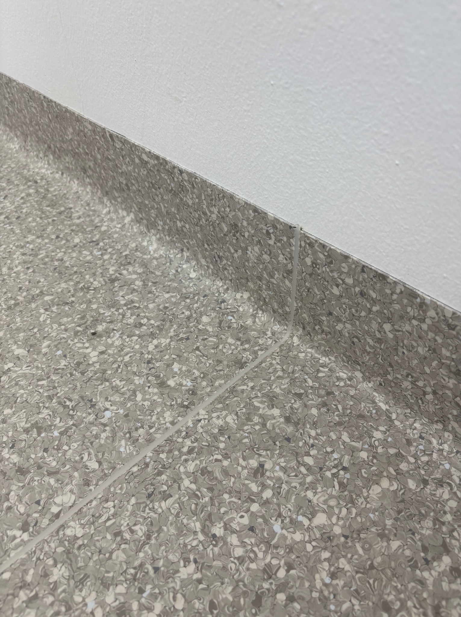 Szara, wzorzysta podłoga z listwą przypodłogową, świeżo po montażu. Widoczne łączenie między panelami i ściana w tle. Ujęcie z bliska.