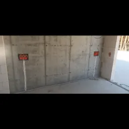 Surowa ściana z betonu z widocznymi puszkami elektrycznymi i przewodami w peszlu, instalacja w trakcie montażu.