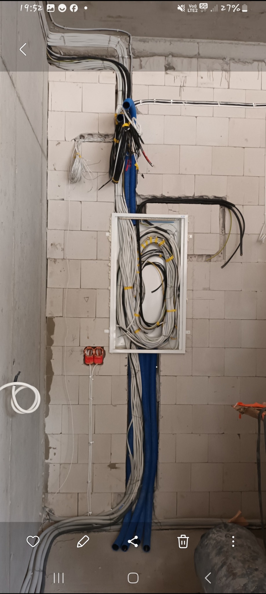 Rozprowadzenie przewodów elektrycznych w ścianie z betonu komórkowego, widoczna skrzynka rozdzielcza z uporządkowanymi kablami, peszle w kolorze niebieskim i szarym, instalacja w trakcie realizacji.