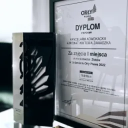 Dyplom w czarnej ramie dla kancelarii adwokackiej Wiktorii Zawadzkiej za zajęcie I miejsca w zestawieniu Orły Prawa 2022, obok statuetka z napisem 1 Miejsce 2022