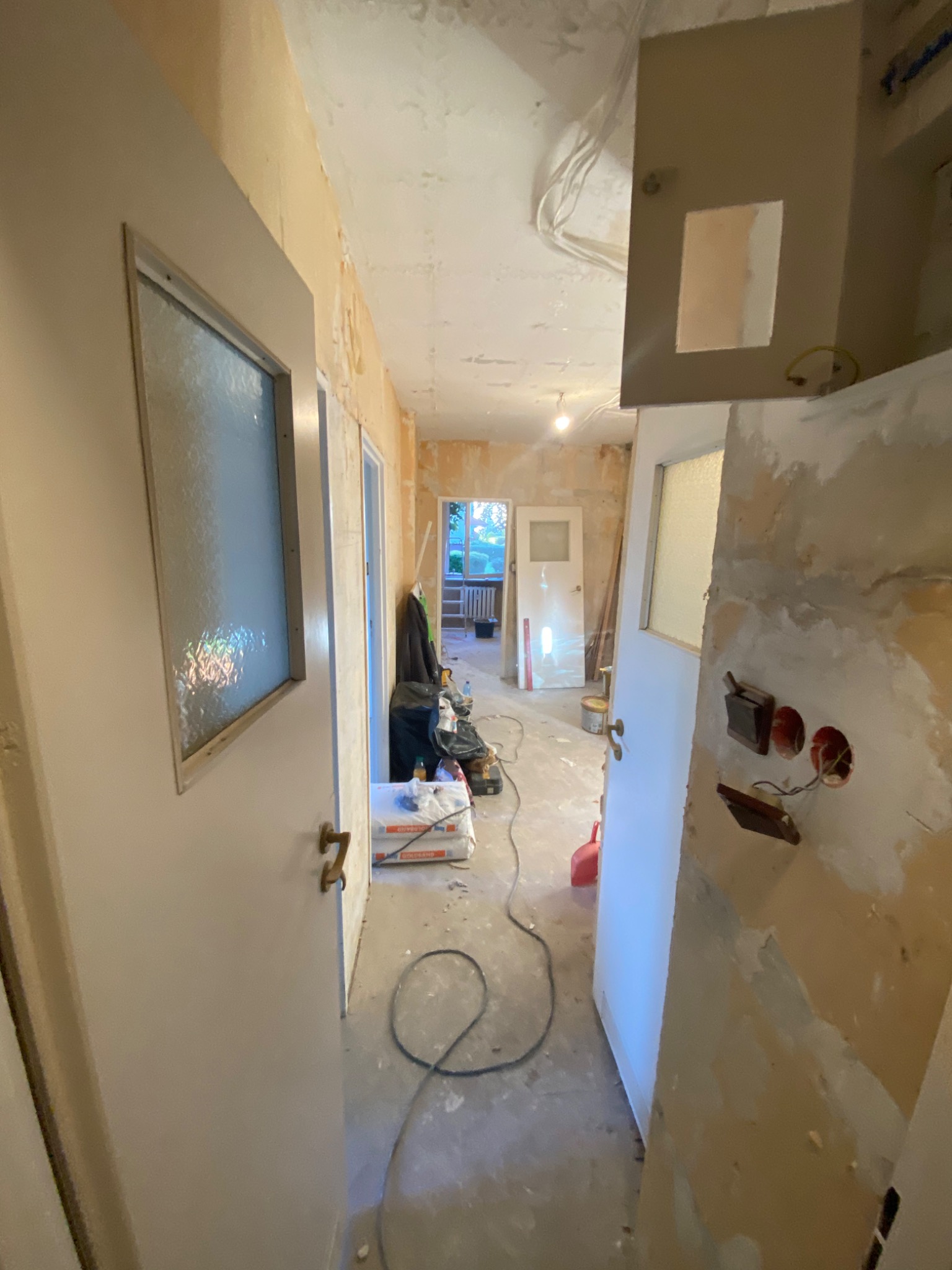 Wnętrze mieszkania w Strzegomiu w trakcie prac wykończeniowych: ściany przygotowane do malowania, widoczne puszki elektryczne i kable, częściowo odnowione drzwi z szybą. Na podłodze widoczne...