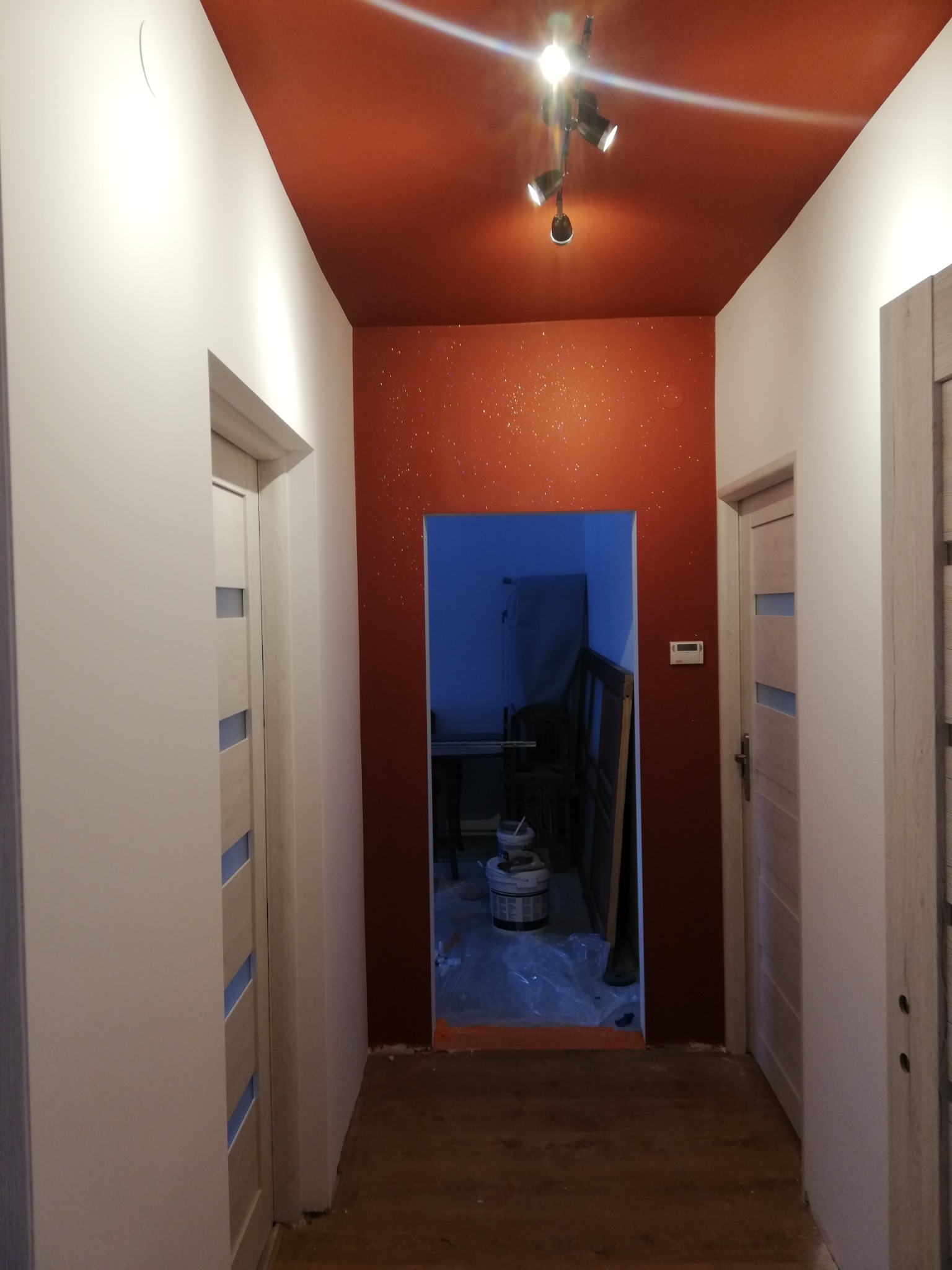 Korytarz po malowaniu w Pewel Ślemieńska: ściany białe, sufit w odcieniach czerwieni z dekoracyjnymi drobinkami, widoczne drzwi i podłoga w odcieniach brązu, w głębi pomieszczenia widoczne...