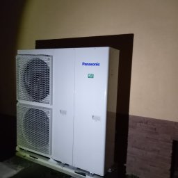 MARGO SOLAR ENERGY - MARIAN MAZUR - Biała, dwuczęściowa jednostka zewnętrzna z logo Panasonic i oznaczeniem R32, zamontowana przy ścianie budynku z elementami dekoracyjnymi, w zimowych warunkach.