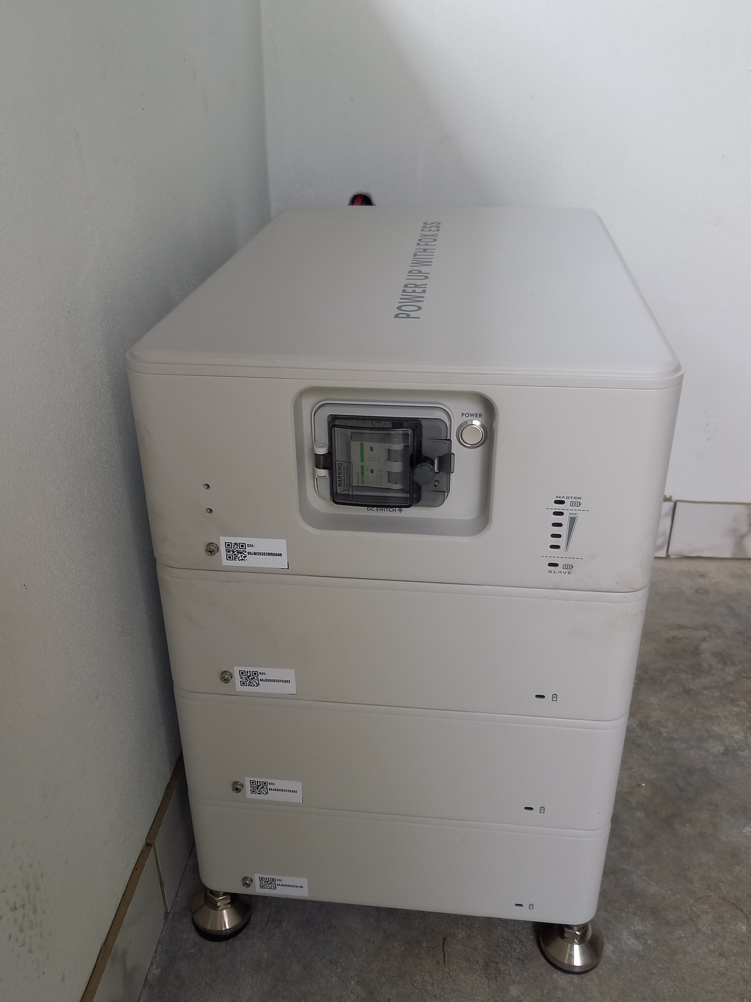 Biały, modułowy magazyn energii Fox ESS z widocznym wyłącznikiem DC, umieszczony w pomieszczeniu w Raba Wyżna, z widocznymi naklejkami z kodami QR i regulowanymi nóżkami.