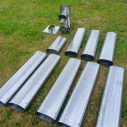 Elementy systemu odprowadzania spalin kominka, w tym rury i trójnik, rozłożone na trawie przed montażem.