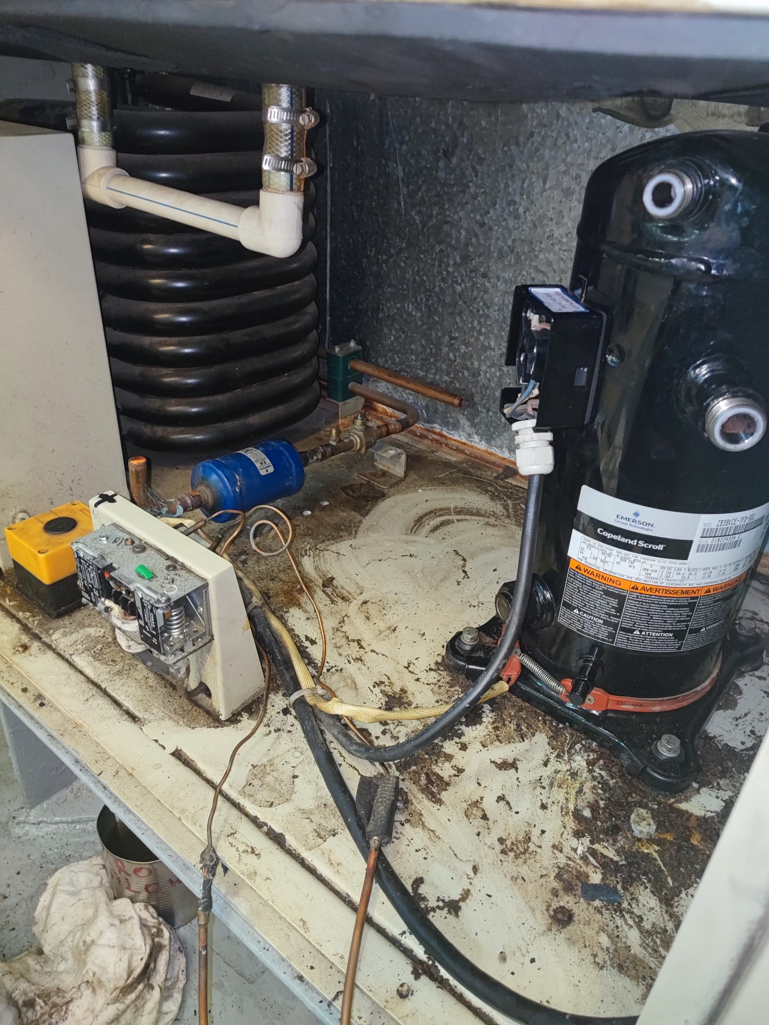 Sprężarka chłodnicza Emerson Copeland Scroll z widocznymi przewodami, elementami elektrycznymi i rurami miedzianymi w przestrzeni technicznej, prawdopodobnie podczas serwisu.