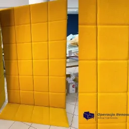 Żółty, modułowy panel akustyczny z kwadratowymi przeszyciami, widoczne 3 fragmenty, tło warsztatowe.