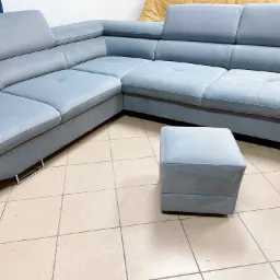 Narożnik tapicerowany w odcieniach błękitu z pufą na kafelkowej podłodze, widoczne metalowe nóżki