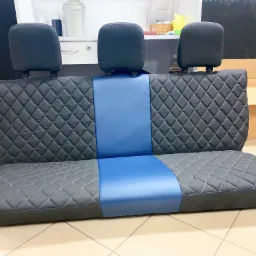 Odnowione tylne siedzenie samochodowe z trzema zagłówkami, wykończone czarną pikowaną tkaniną z niebieskim pasem pośrodku, widoczne na jasnej podłodze.